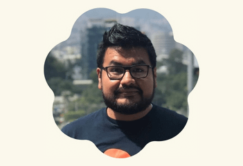 Portrait of Carlos from Mexico team wearing glasses and a navy t-shirt, framed in a decorative scalloped floral shape.