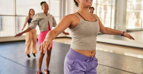 Quatro pessoas com roupas esportivas sorriem e se exercitam juntas em um estúdio de dança bem iluminado.