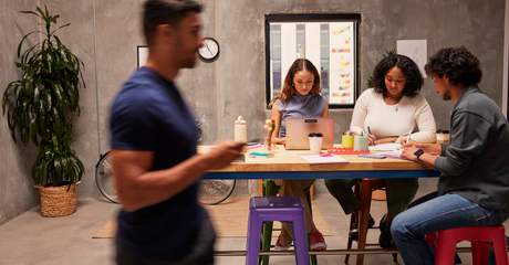 Colaboradores reunidos em um espaço de trabalho colaborativo, trocando ideias em equipe enquanto utilizam laptop e anotações para desenvolver projetos.