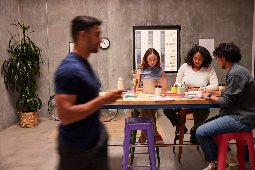 Colaboradores reunidos em um espaço de trabalho colaborativo, trocando ideias em equipe enquanto utilizam laptop e anotações para desenvolver projetos.