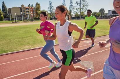 Grupo de pessoas correndo em pista de atletismo ao ar livre, praticando corrida como exercício físico para saúde, resistência e bem-estar.