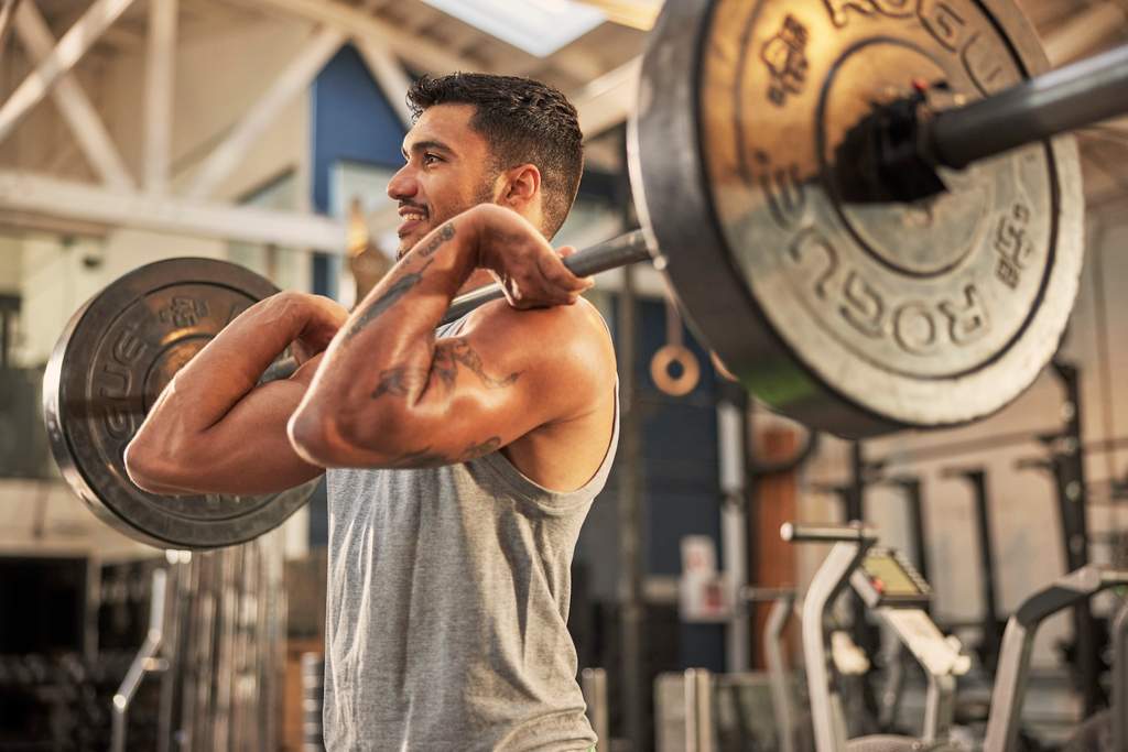 Homem realizando exercício de levantamento de barra em academia, fortalecendo braços e costas durante treino de musculação.