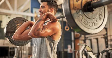 Homem realizando exercício de levantamento de barra em academia, fortalecendo braços e costas durante treino de musculação.