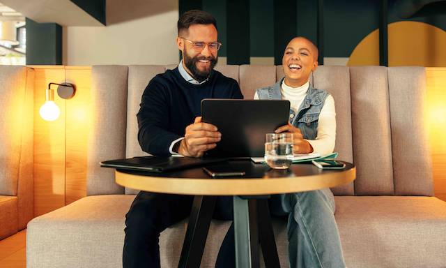 Two coworkers laughing while looking at a computer screen.