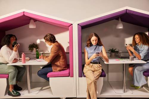 Four professionals working and using phones inside modern, colorful office meeting pods.