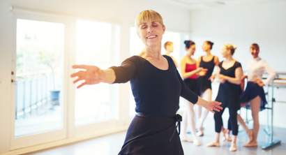Pessoa adulta em aula de ballet em estúdio, realizando exercício de barra com postura alinhada e foco na técnica