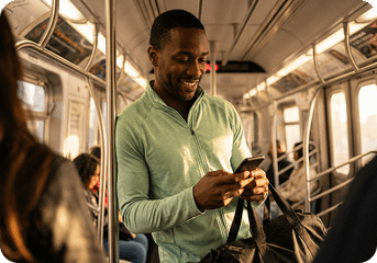 A man smiling while looking at his phone while commuting on a New York City subway train.