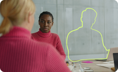 A black woman in a pink turtleneck sits at a table across from another person, with a neon-green outline of a missing person seated next to them.