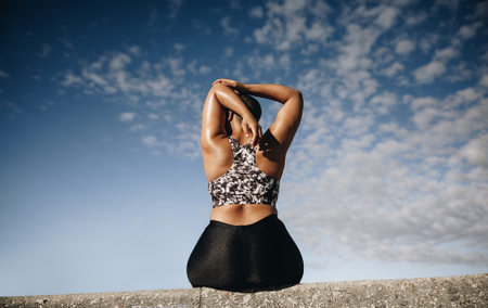 Woman sitting down, showing her back to the camera, stetching.