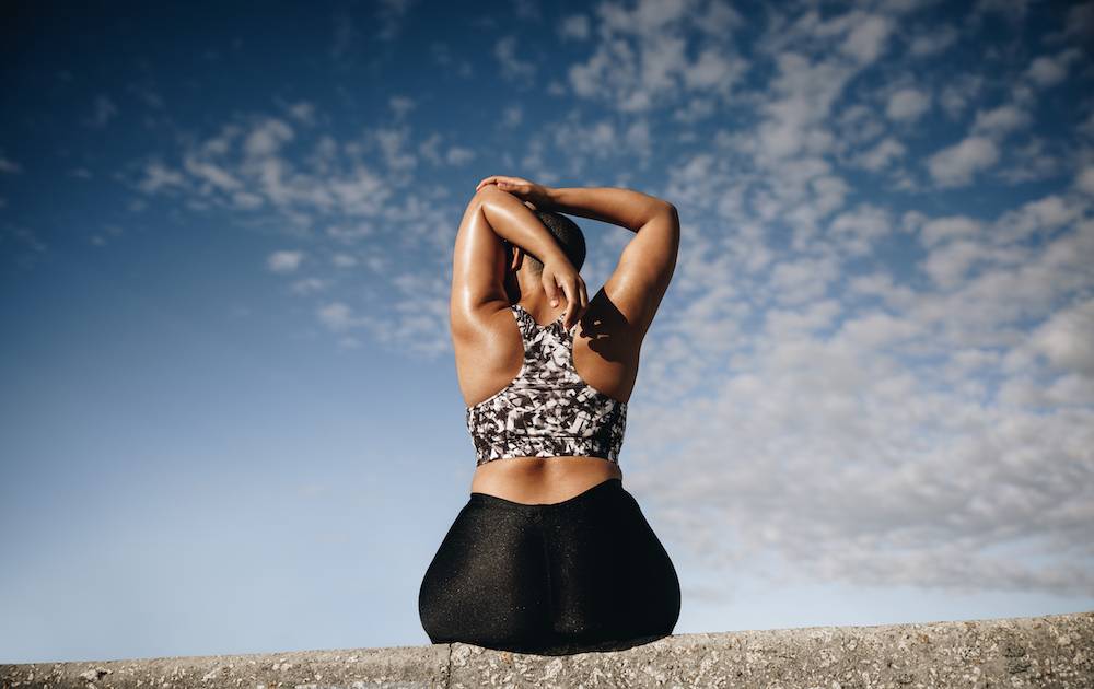 Woman sitting down, showing her back to the camera, stetching.