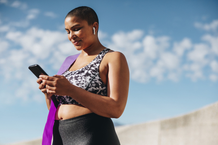 Woman standing up, wearing gym clothes, holding a cellphone, looking down.