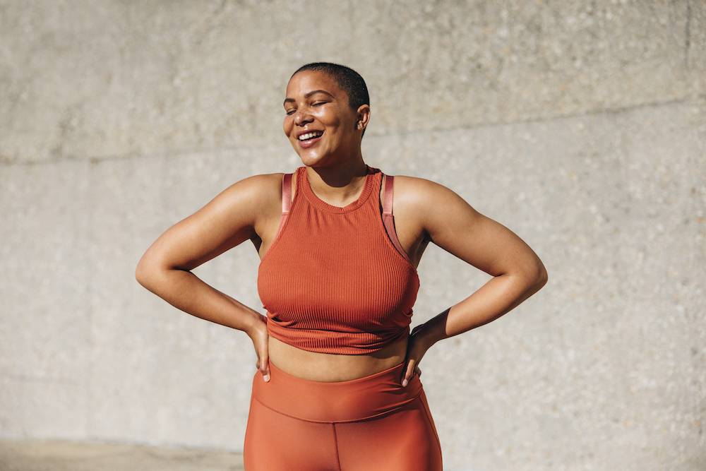 Woman standing up, wearing gym clothes, smiling with her eyes closed.