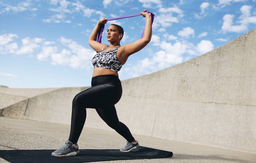 Woman standing up, wearing gym clothes, stretching.