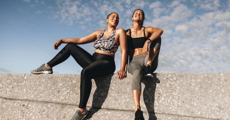 Two women sitting down, wearing gym clothes, laughing.