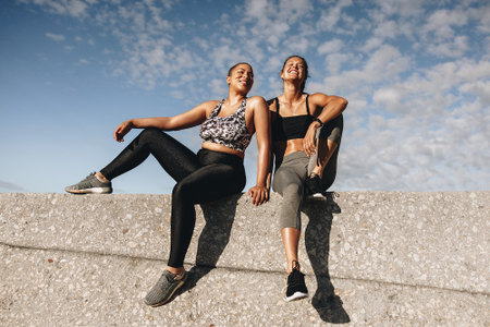 Two women sitting down, wearing gym clothes, laughing.