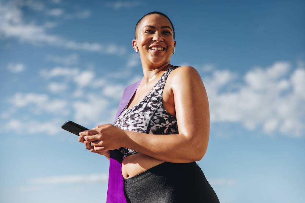 Woman standing up, holding a cellphone, smiling.