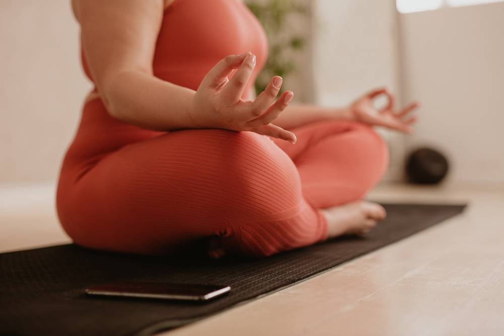 Woman sitting on the floor, wearing gym clothes, in a meditation pose.