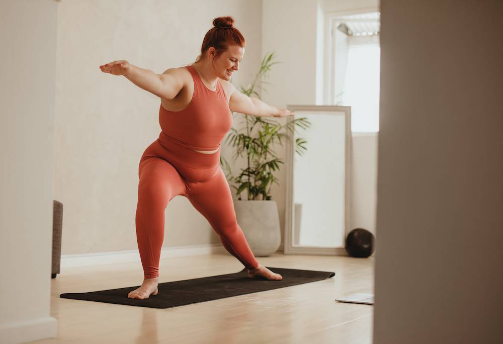 Woman standing up, wearing gym clothes, practicing yoga.