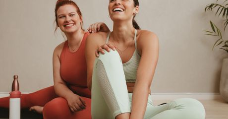 Two women sitting on the floor, wearing gym clothes, laughing.