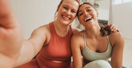 Two women taking a selfie, laughing, wearing gym clothes.