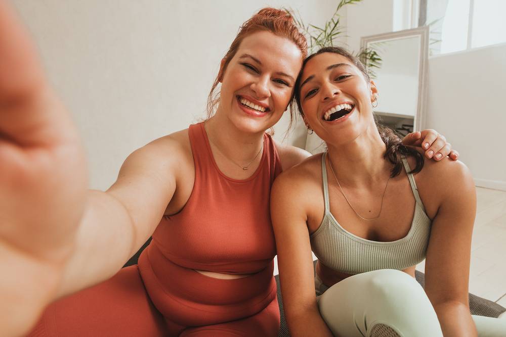 Two women taking a selfie, laughing, wearing gym clothes.