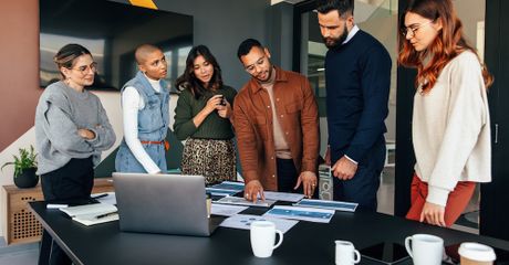 Six people working while they stand at a conference table