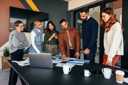 Six people working while they stand at a conference table