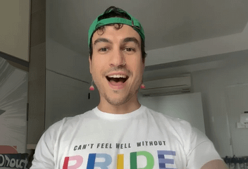 A person wearing a green cap and a white t-shirt that reads "Can't feel well without Pride" in rainbow letters.
