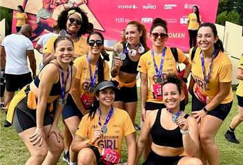 A group of smiling women posing with medals in front of a pink backdrop after a "Girl" marathon event.